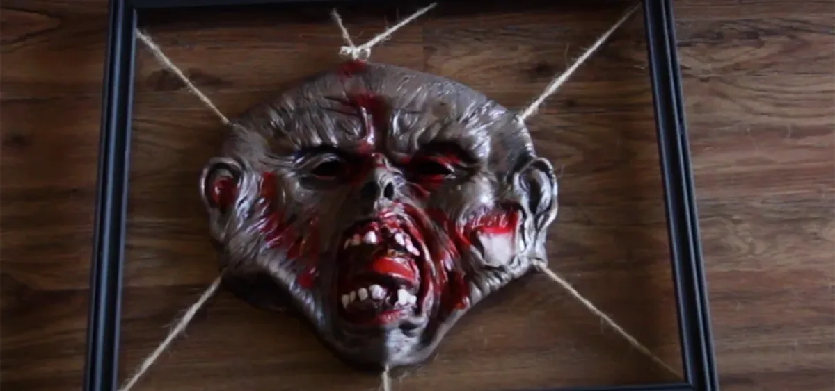 A stretched zombie mask framed with twine as gruesome wall art
