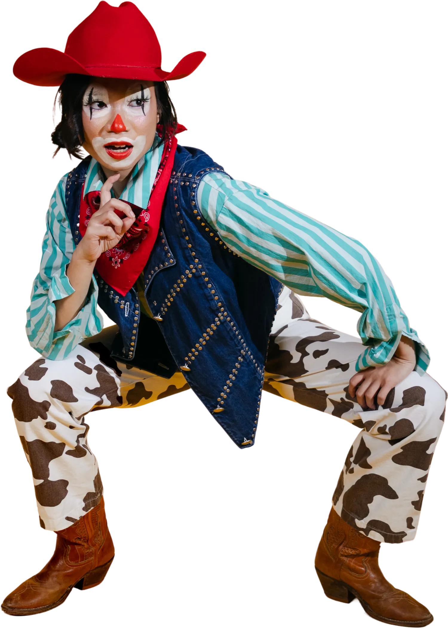 A model in a rodeo clown costume — cow-print jeans, denim vest, striped shirt and a red felt hat — crouched wide, pointing at the camera.